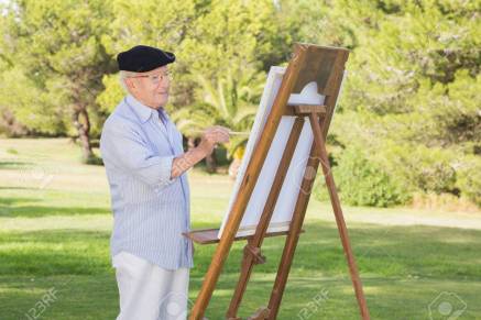 Old man wearing a beret painting in the park using an easel